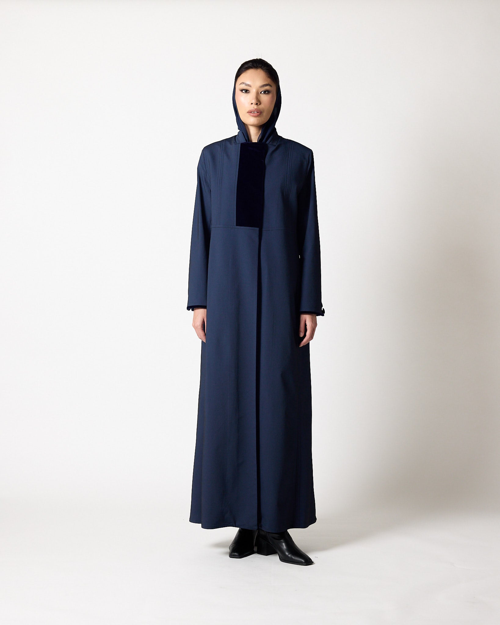 A model stands facing forward wearing a long navy blue hooded abaya with a contrasting dark navy velvet chest panel and black pointed shoes, photographed against a neutral light gray studio background.عبايات قطر | Abaya Qatar
عبايات الدوحة | Abayas Doha
عباية قطر | Abaya Doha
عبايات اونلاين قطر | Abayas Online Qatar
عبايات أونلاين قطر | Online Abayas Qatar
شراء عبايات قطر | Buy Abaya Qatar
شراء عبايات اونلاين | Buy Abayas Online
متجر عبايات قطر | Abaya Store Qatar
محل عبايات قطر | Abaya Shop Qatar
بوتيك عبا