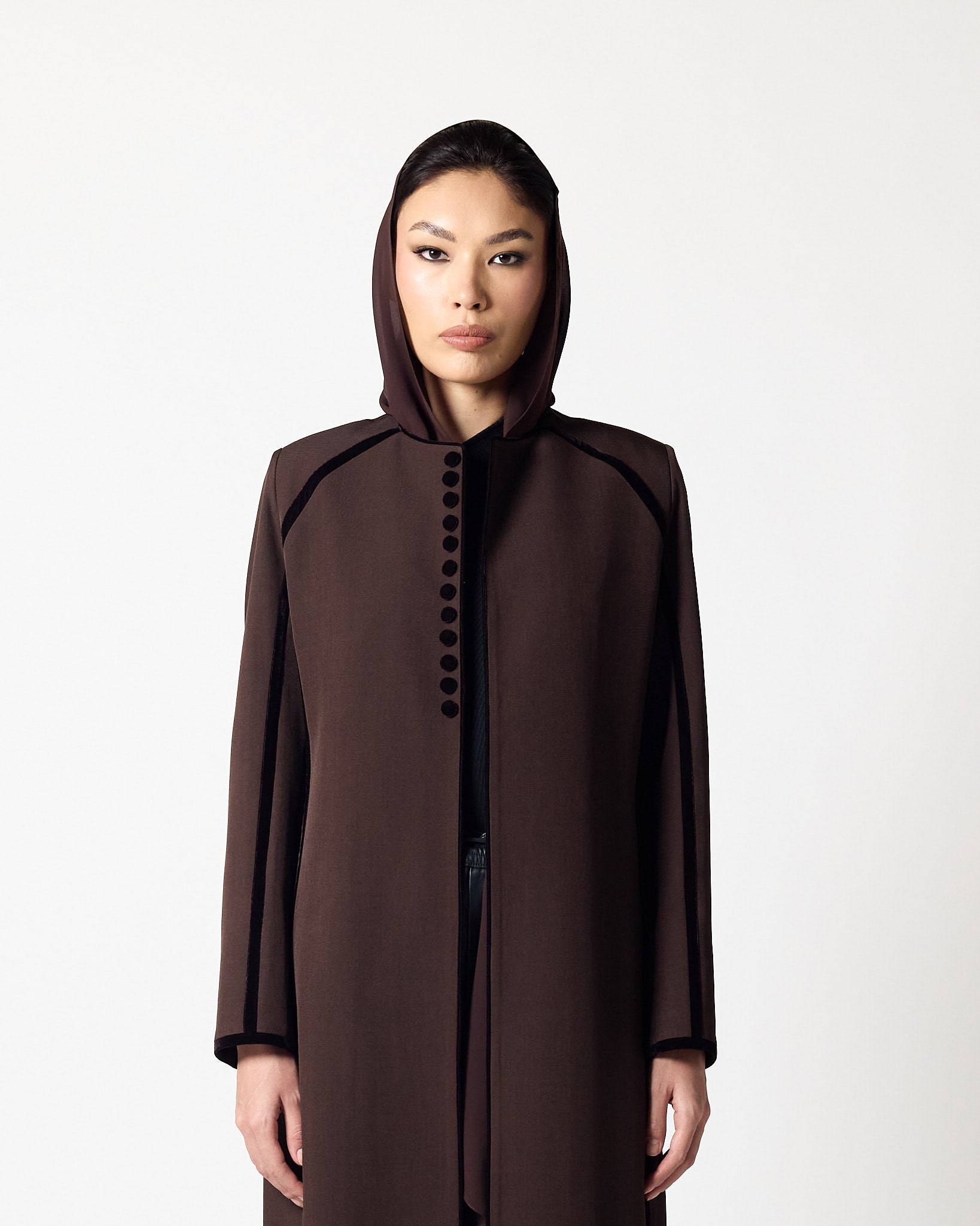 A model wearing a dark brown hooded coat with black trim and a row of black buttons down the front, photographed against a plain light gray background.عبايات قطر | Abaya Qatar
عبايات الدوحة | Abayas Doha
عباية قطر | Abaya Doha
عبايات اونلاين قطر | Abayas Online Qatar
عبايات أونلاين قطر | Online Abayas Qatar
شراء عبايات قطر | Buy Abaya Qatar
شراء عبايات اونلاين | Buy Abayas Online
متجر عبايات قطر | Abaya Store Qatar
محل عبايات قطر | Abaya Shop Qatar
بوتيك عبايات قطر | Abaya Boutique Qatar
عبايات نسائية قطر |